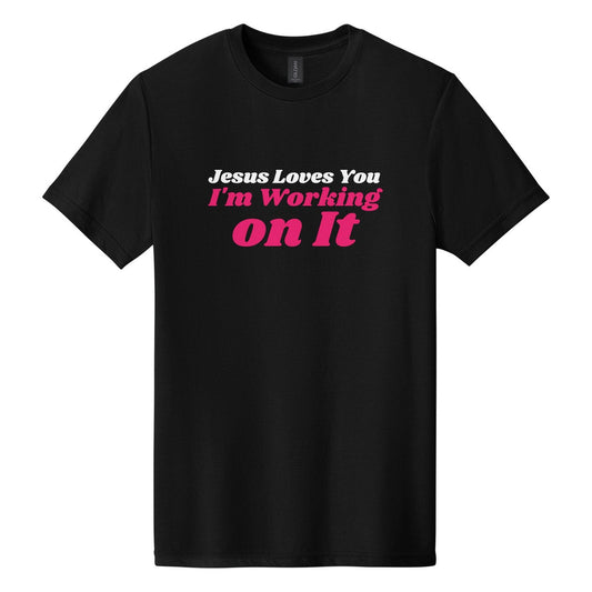 Jesus Loves You. I'm Working on It tee in Pitch Black, Shrikhand font, White + Hot Pink ink
